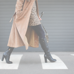 Woman wearing cheetah print dress, brown trench coat, and leather boots