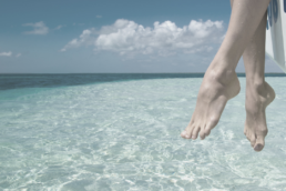 Close up of woman's feet hanging off a boat in a clear blue ocean