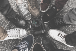 11 people standing with one foot in the middle of a circle with a Canon camera in the center