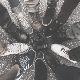 11 people standing with one foot in the middle of a circle with a Canon camera in the center