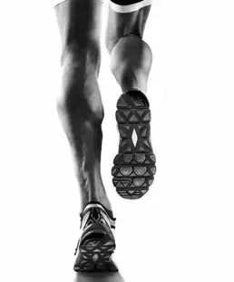 Black and white close up shot of male athlete's calf muscles in mid-run