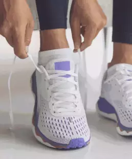 Close up shot of woman lacing up white and purple tennis shoes